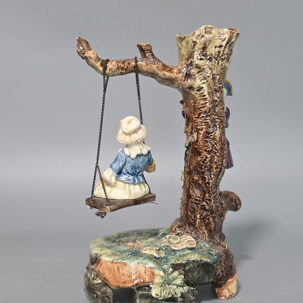 A Victorian majolica spill holder shaped as a hollow tree trunk with a figure of a man playing a lute next to a woman suspended on a swing. View III