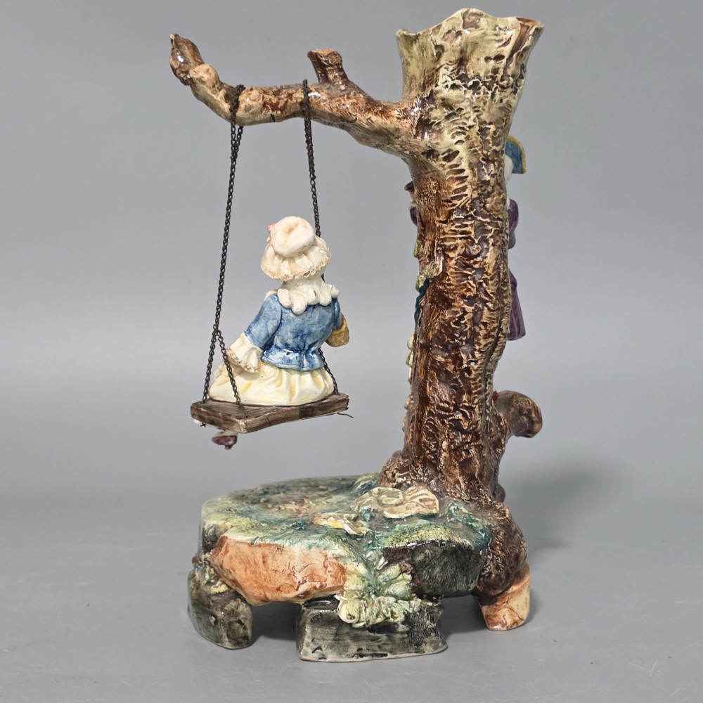 A Victorian majolica spill holder shaped as a hollow tree trunk with a figure of a man playing a lute next to a woman suspended on a swing. View IV