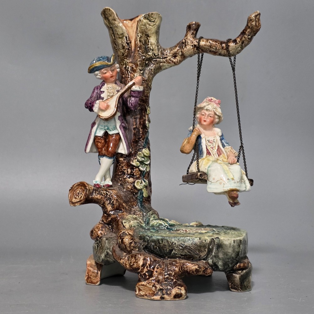 A Victorian majolica spill holder shaped as a hollow tree trunk with a figure of a man playing a lute next to a woman suspended on a swing. View VI
