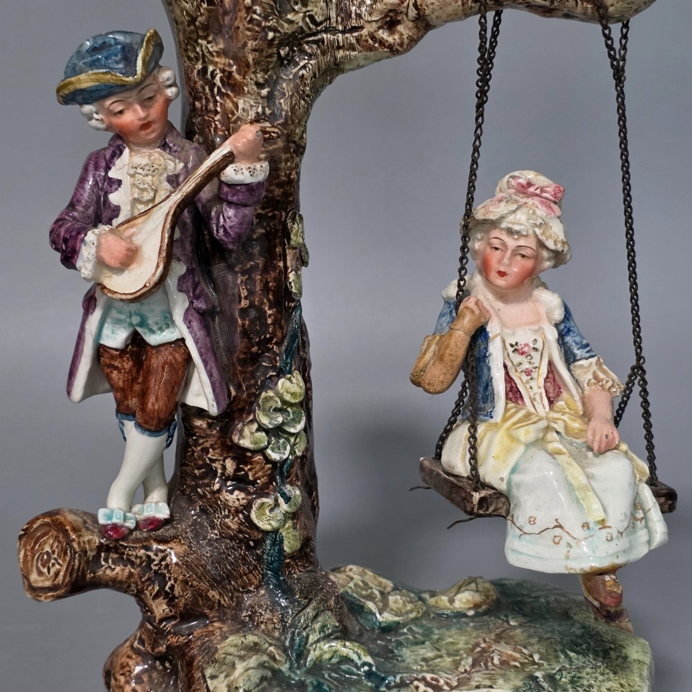 A Victorian majolica spill holder shaped as a hollow tree trunk with a figure of a man playing a lute next to a woman suspended on a swing. View VII