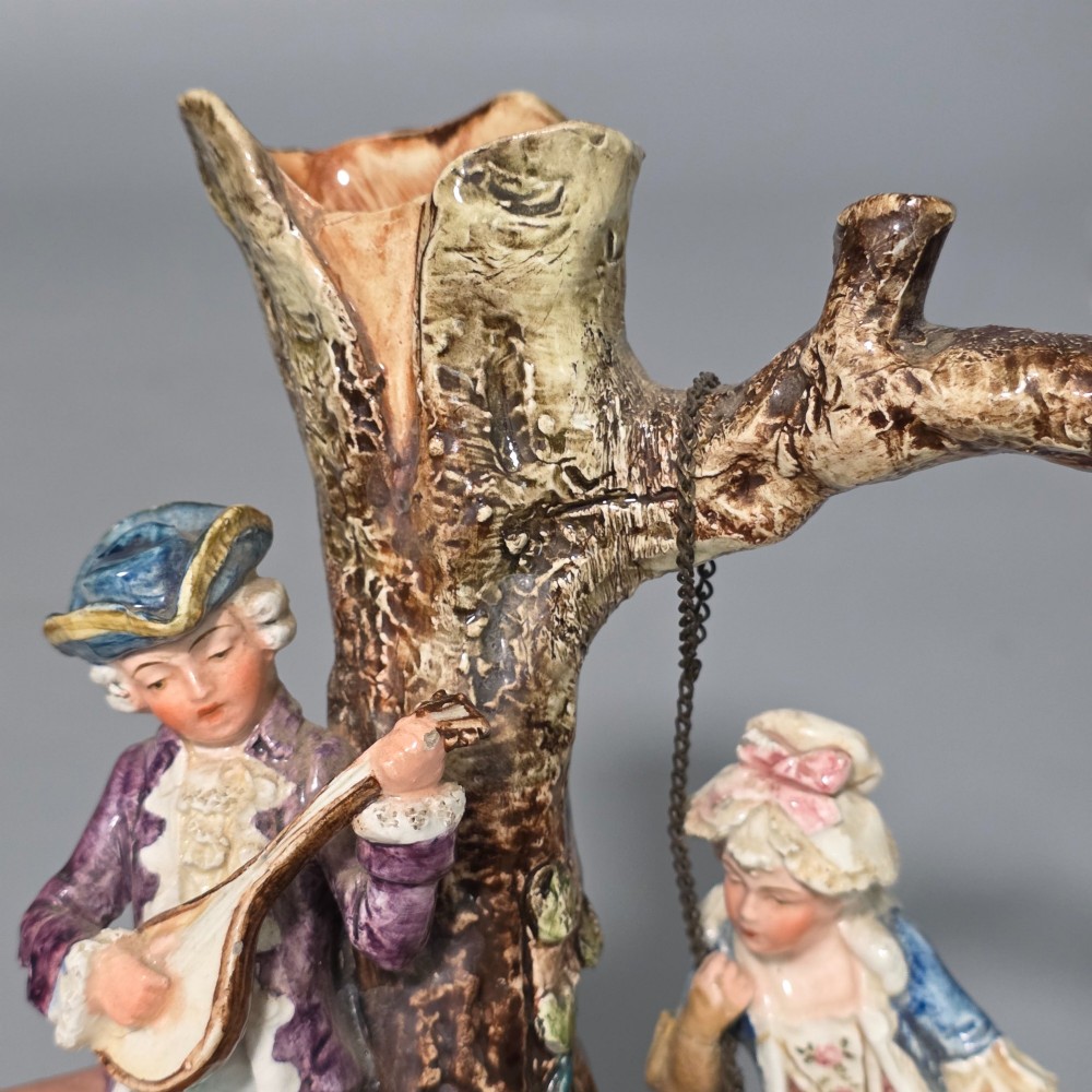 A Victorian majolica spill holder shaped as a hollow tree trunk with a figure of a man playing a lute next to a woman suspended on a swing. View VIII