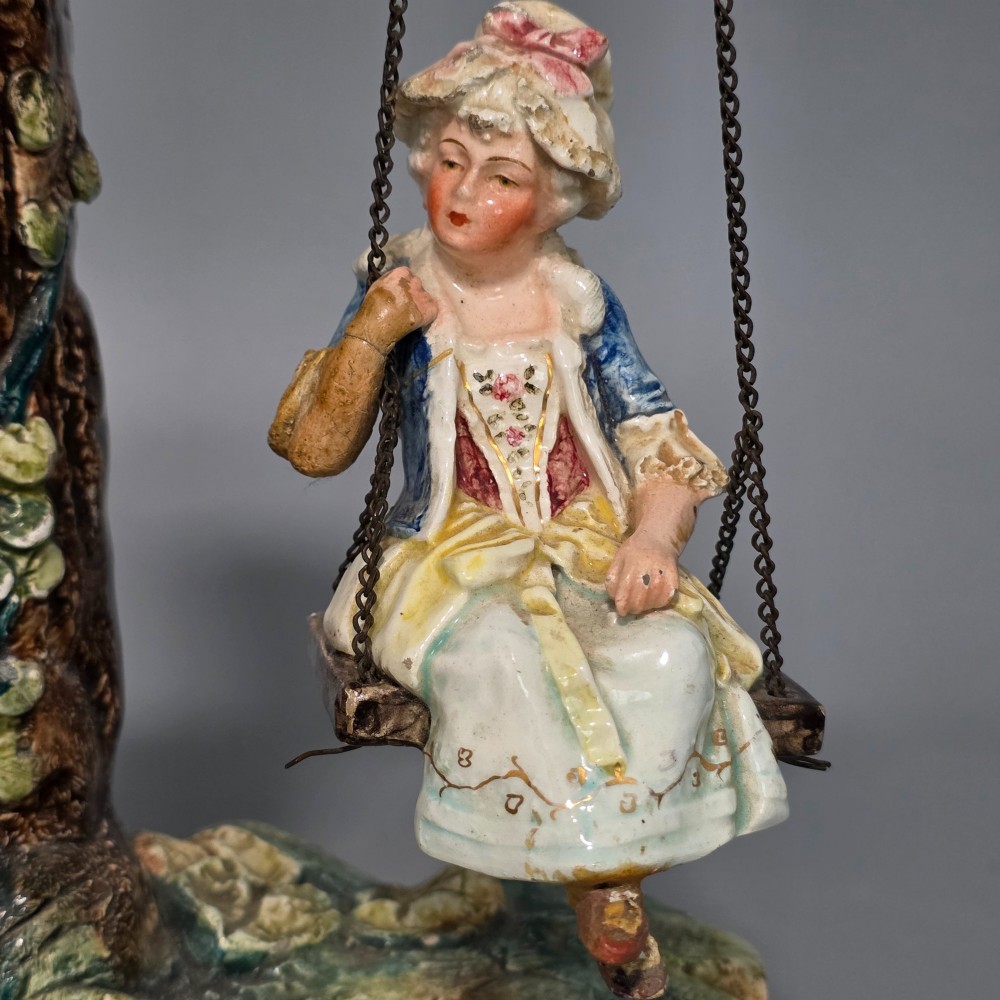 A Victorian majolica spill holder shaped as a hollow tree trunk with a figure of a man playing a lute next to a woman suspended on a swing. View IX