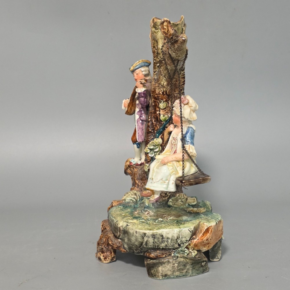 A Victorian majolica spill holder shaped as a hollow tree trunk with a figure of a man playing a lute next to a woman suspended on a swing. View X