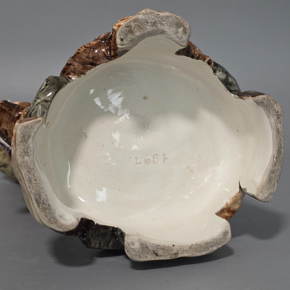 A Victorian majolica spill holder shaped as a hollow tree trunk with a figure of a man playing a lute next to a woman suspended on a swing. View XIII