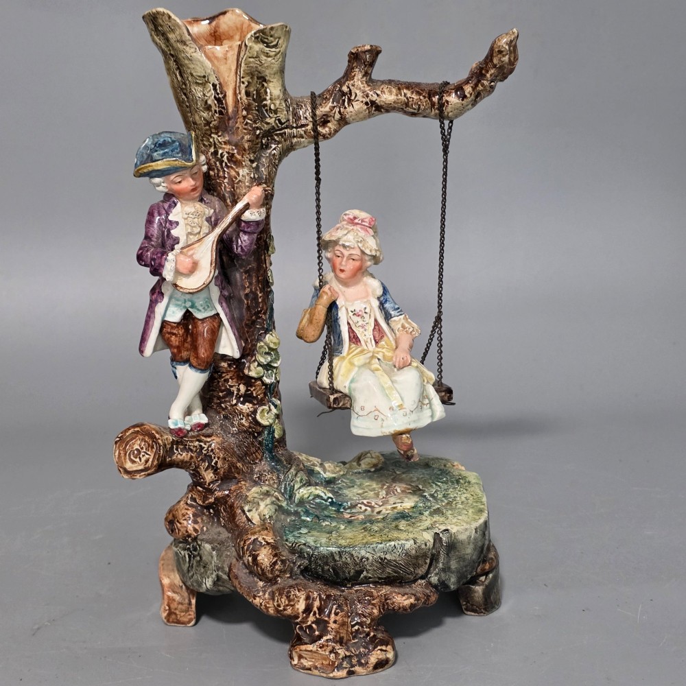 A Victorian majolica spill holder shaped as a hollow tree trunk with a figure of a man playing a lute next to a woman suspended on a swing. View XIV