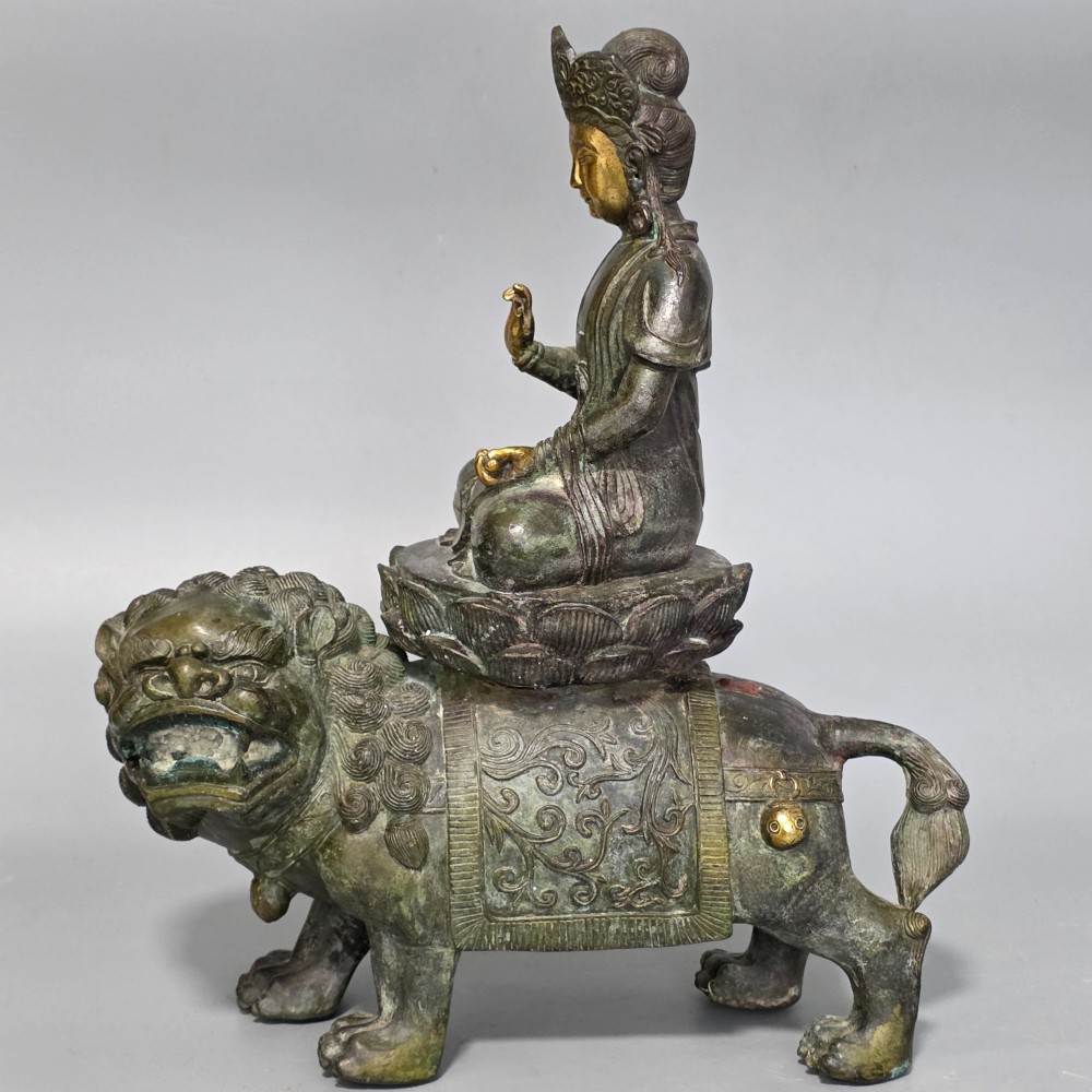 A 19th-century cast bronze sculpture depicting a seated Guanyin figure with gilded facial details riding atop a textured Dog of Fo.