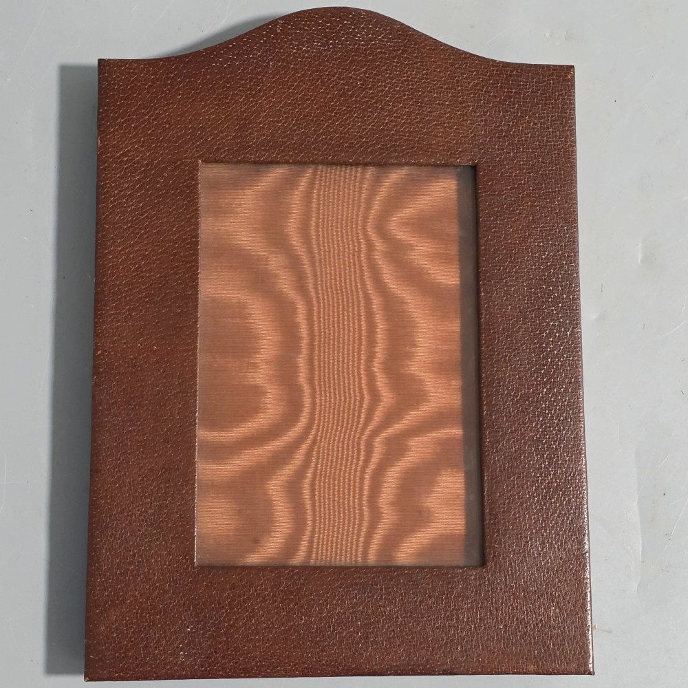 A brown textured leather photo frame featuring an arched top and a central rectangular aperture backed with moire silk. View III