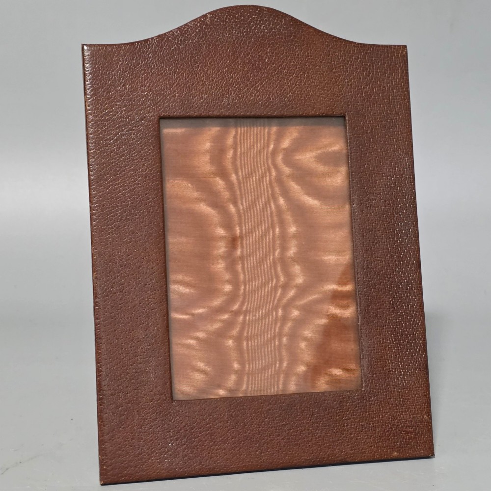 A brown textured leather photo frame featuring an arched top and a central rectangular aperture backed with moire silk. View IV