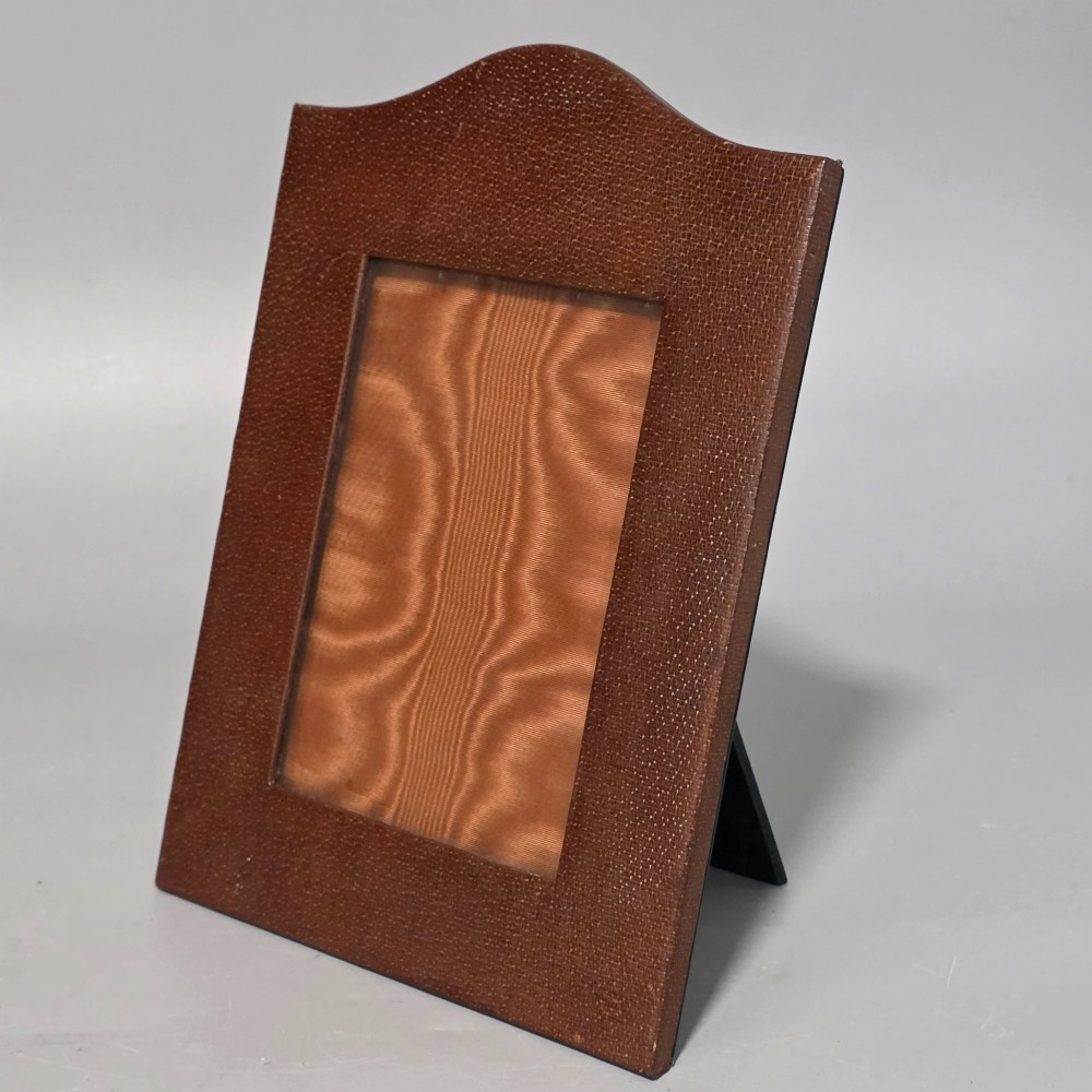 A brown textured leather photo frame featuring an arched top and a central rectangular aperture backed with moire silk. View V