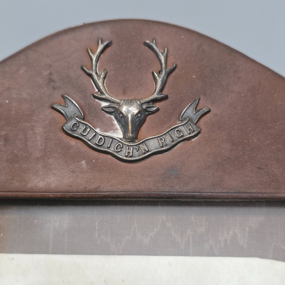 A dark brown leather desktop picture frame featuring an arched top decorated with a metal stag head emblem and motto scroll. View V