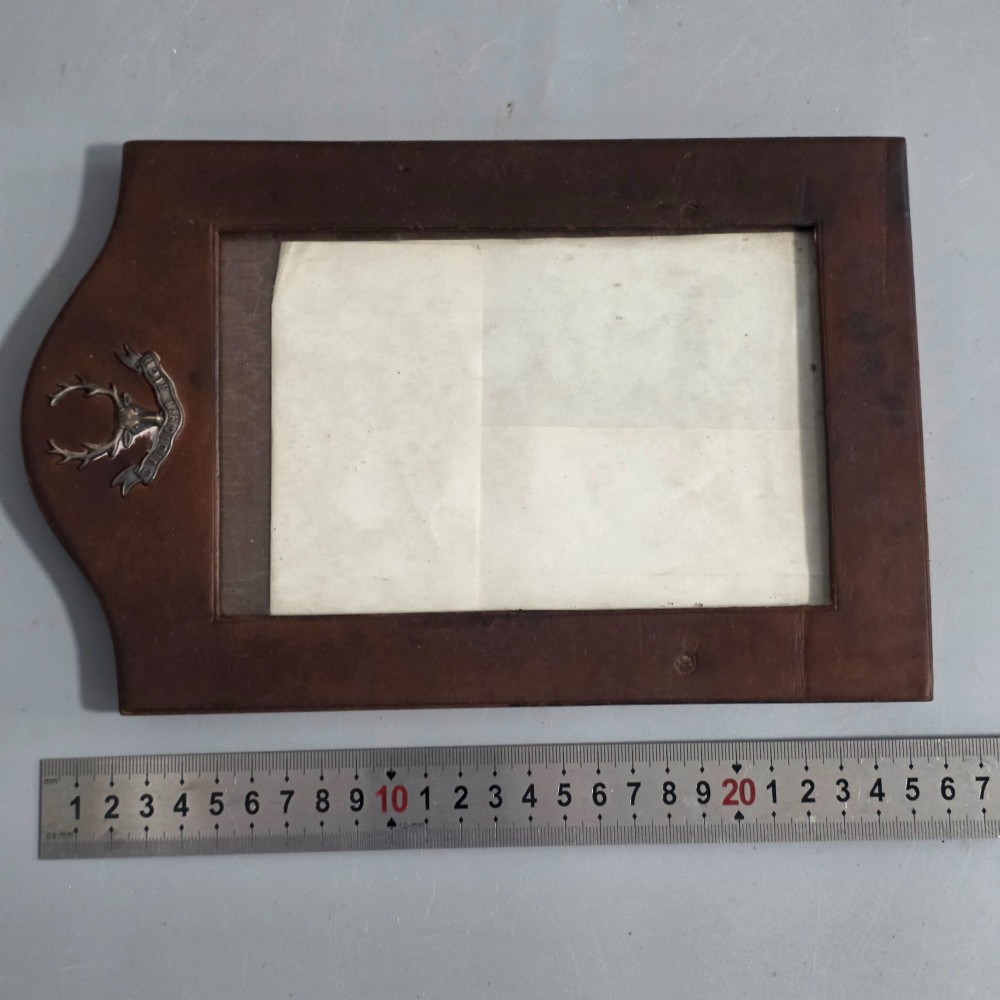A dark brown leather desktop picture frame featuring an arched top decorated with a metal stag head emblem and motto scroll. View VII