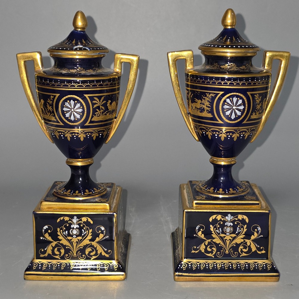 A pair of cobalt blue and gold Vienna porcelain Empire amphora vases featuring hand-painted classical figures and square plinth bases. View X