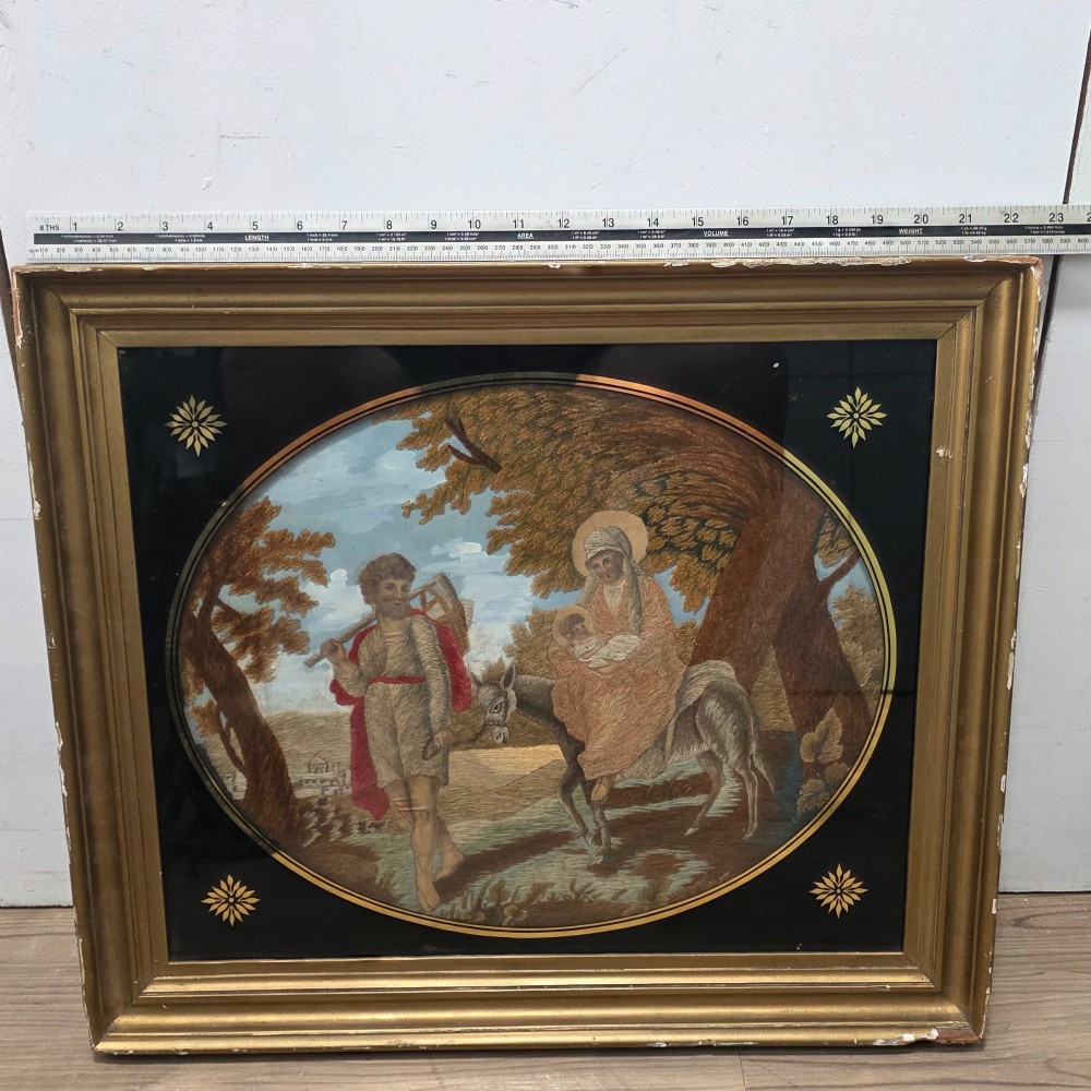 A framed Georgian silkwork and woolwork picture depicting the Flight into Egypt inside an oval glass reserve and a giltwood frame. View II