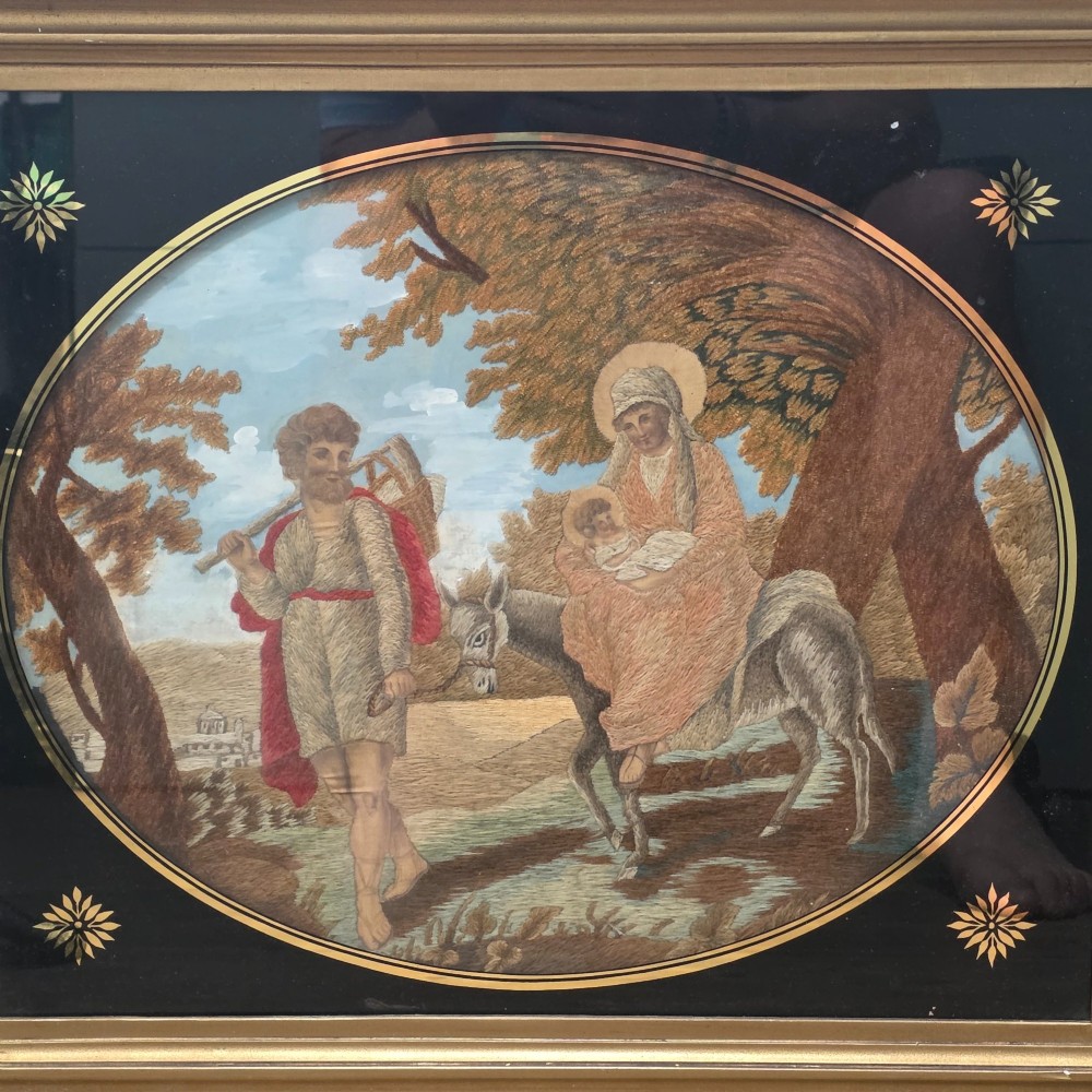A framed Georgian silkwork and woolwork picture depicting the Flight into Egypt inside an oval glass reserve and a giltwood frame. View III