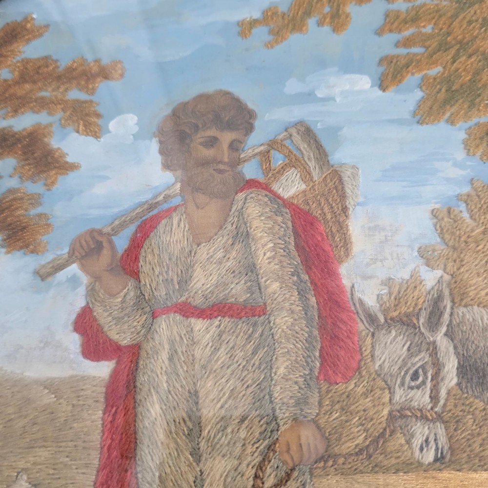 A framed Georgian silkwork and woolwork picture depicting the Flight into Egypt inside an oval glass reserve and a giltwood frame. View XII