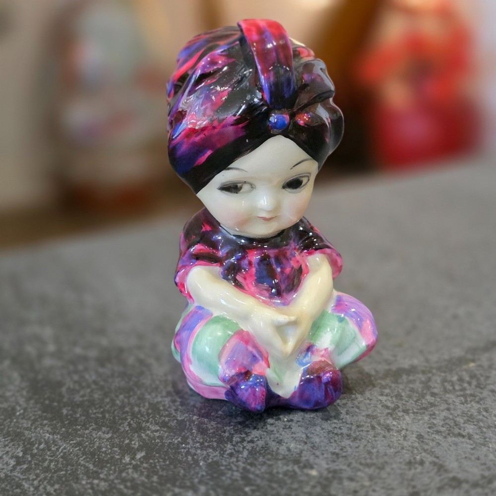 A small glazed ceramic figurine depicting a seated child wearing a patterned purple turban. View III