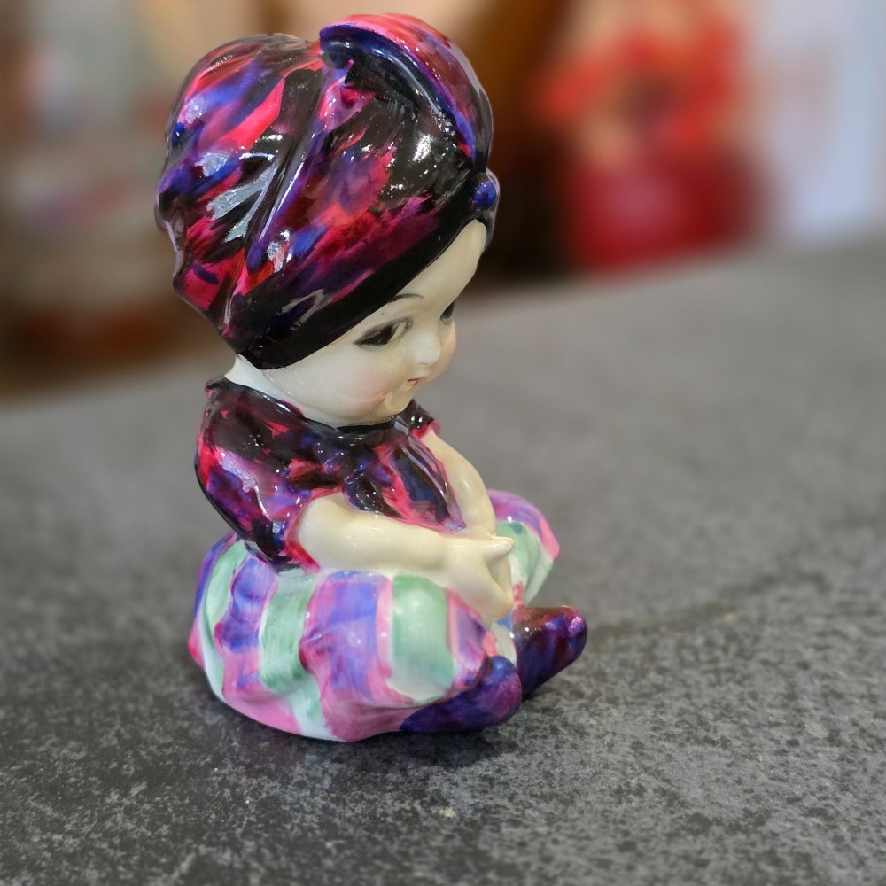 A small glazed ceramic figurine depicting a seated child wearing a patterned purple turban. View IV
