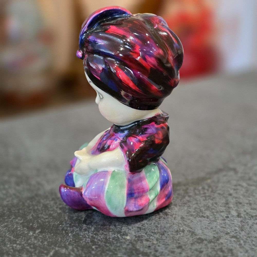 A small glazed ceramic figurine depicting a seated child wearing a patterned purple turban. View VI