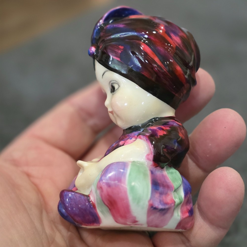 A small glazed ceramic figurine depicting a seated child wearing a patterned purple turban. View IX