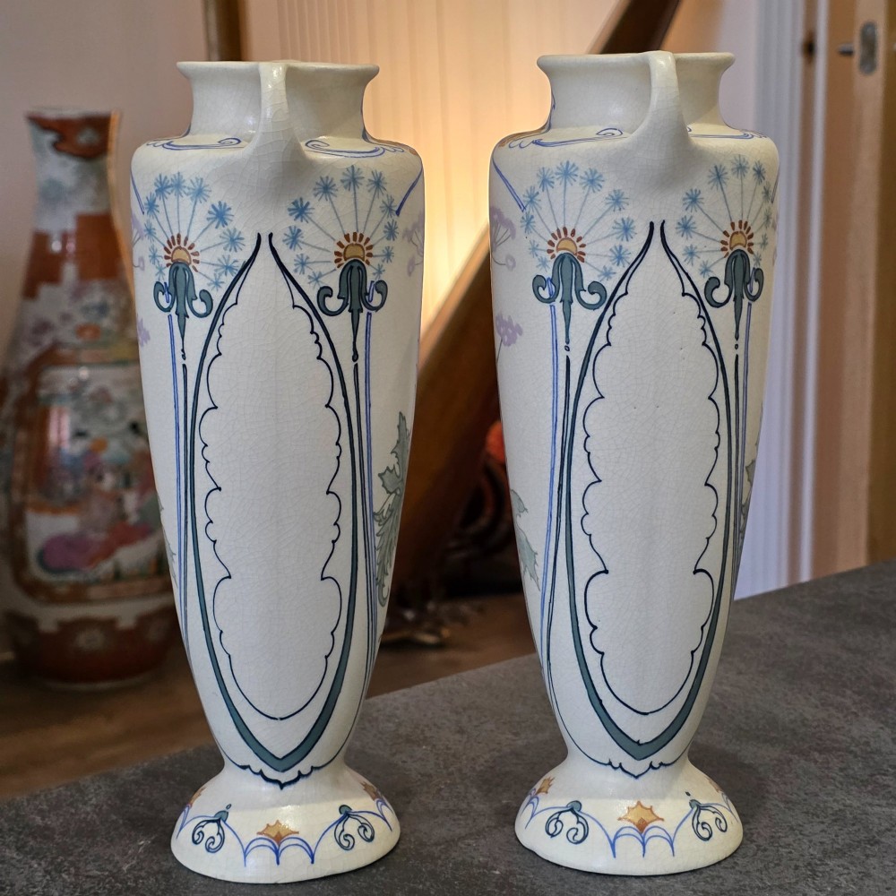 A pair of tall cream ceramic Art Nouveau vases featuring integral twin handles and hand-painted purple and green stylised floral motifs. View II