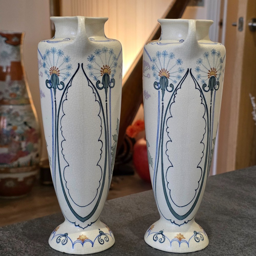 A pair of tall cream ceramic Art Nouveau vases featuring integral twin handles and hand-painted purple and green stylised floral motifs. View III