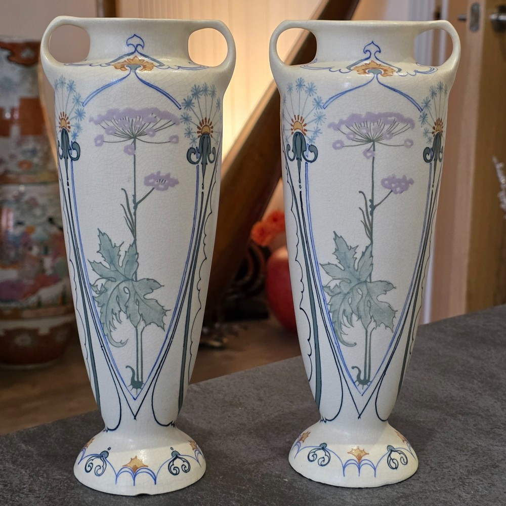 A pair of tall cream ceramic Art Nouveau vases featuring integral twin handles and hand-painted purple and green stylised floral motifs. View IV