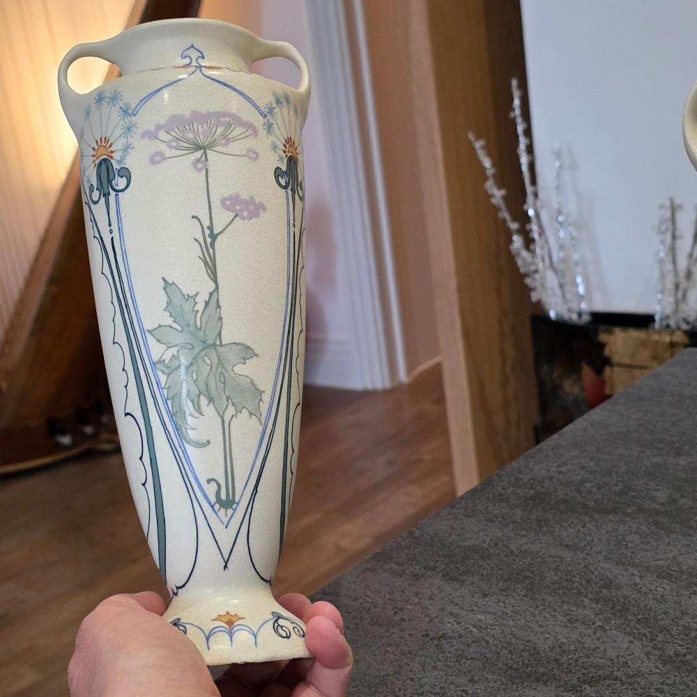 A pair of tall cream ceramic Art Nouveau vases featuring integral twin handles and hand-painted purple and green stylised floral motifs. View IX