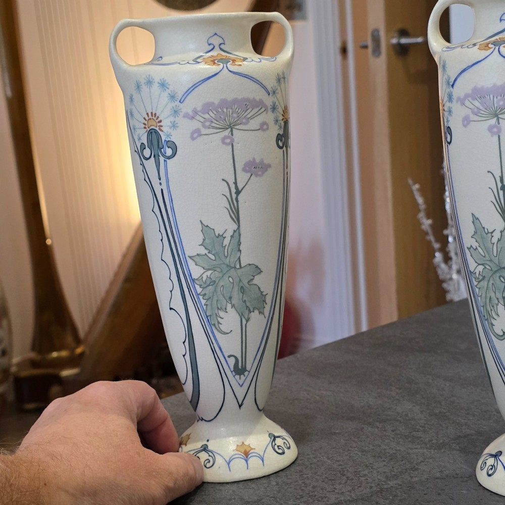 A pair of tall cream ceramic Art Nouveau vases featuring integral twin handles and hand-painted purple and green stylised floral motifs. View XII