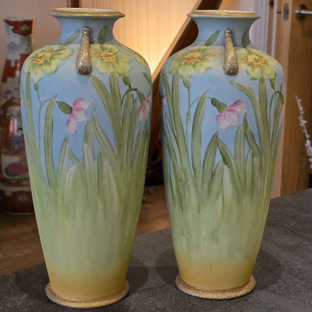 A pair of baluster-shaped porcelain vases featuring hand-painted daffodil and blossom motifs over a light blue and yellow gradient background with small gilded handles.