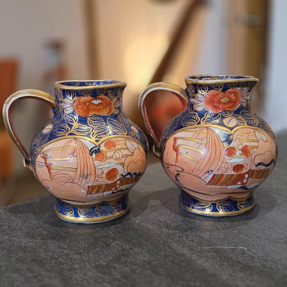 A pair of bulbous stoneware jugs decorated in cobalt blue, terracotta, and gold Imari style patterns with raised handles.