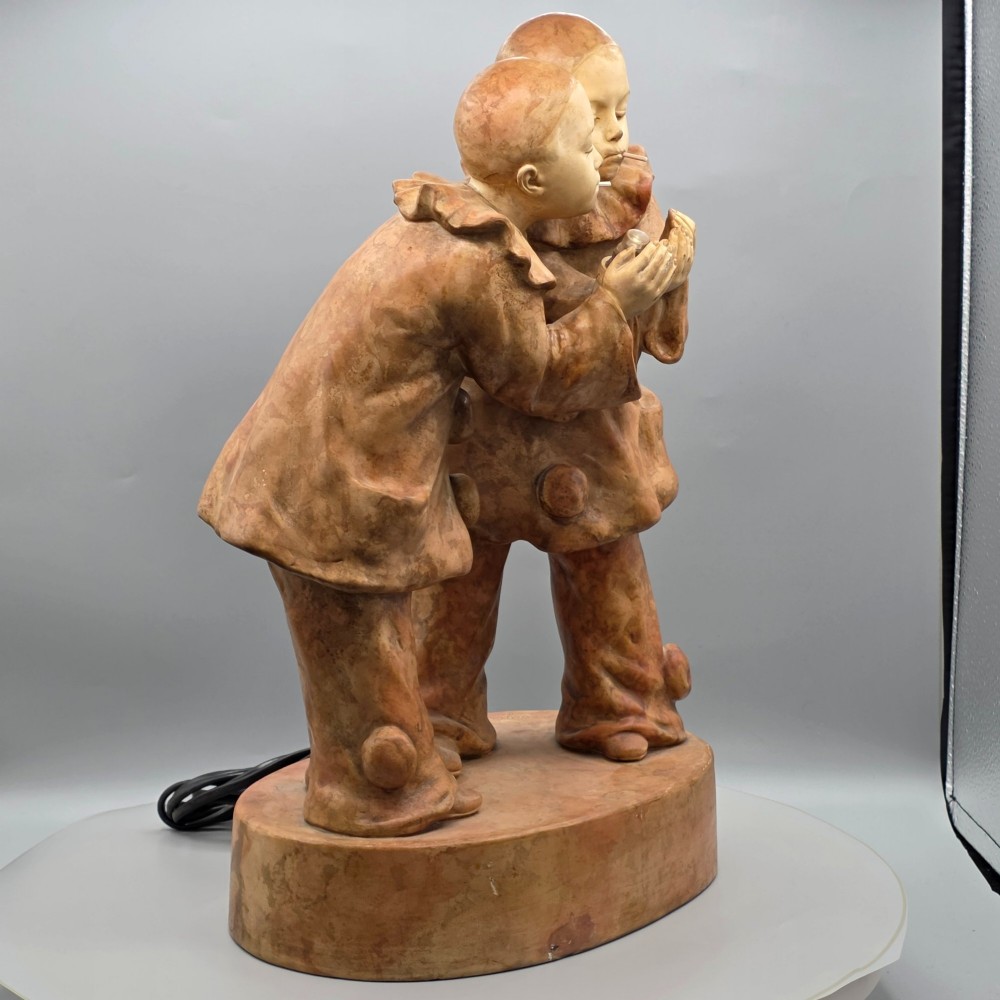 A terracotta sculpture featuring two Pierrot figures in ruffled collars standing together on an oval plinth, designed as a lamp base. View X