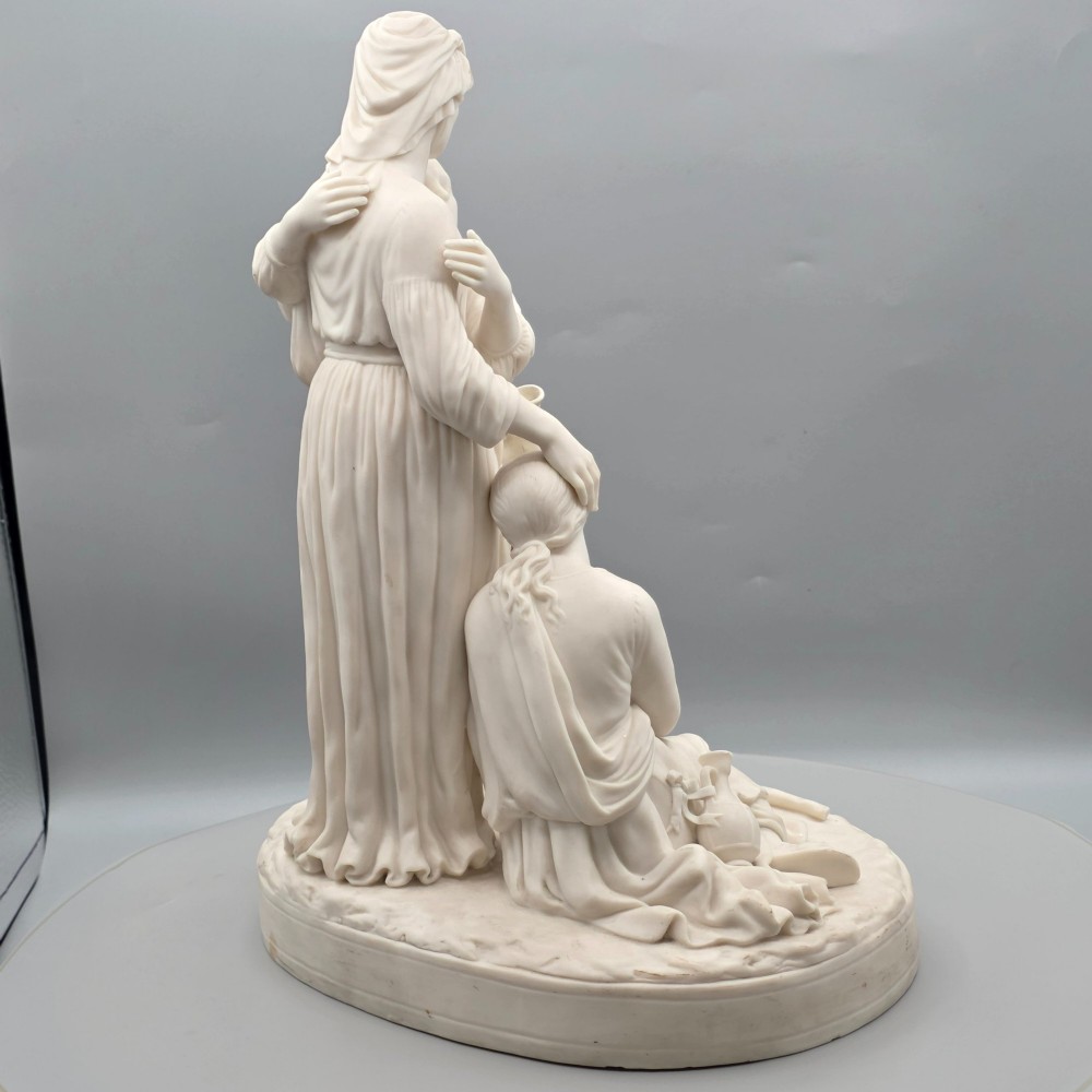 A Victorian off-white parian porcelain figural group depicting three women in classical draped robes on an oval base. View V