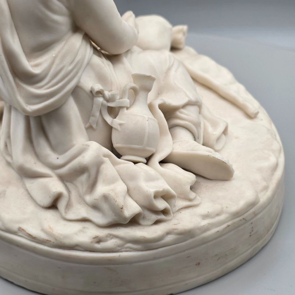 A Victorian off-white parian porcelain figural group depicting three women in classical draped robes on an oval base. View X