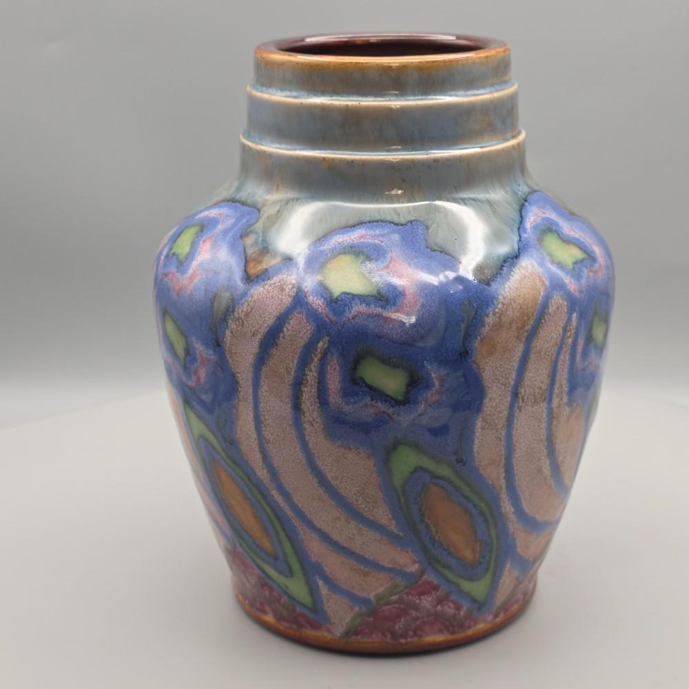 An Art Nouveau baluster-shaped stoneware vase with a stepped rim, featuring vibrant blue, pink, green, and ochre glazes forming abstract floral motifs. View IV