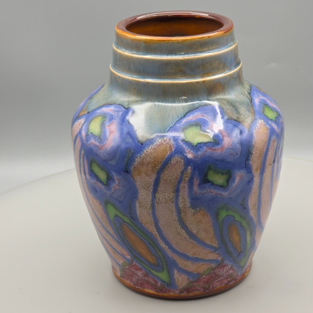 An Art Nouveau baluster-shaped stoneware vase with a stepped rim, featuring vibrant blue, pink, green, and ochre glazes forming abstract floral motifs. View V