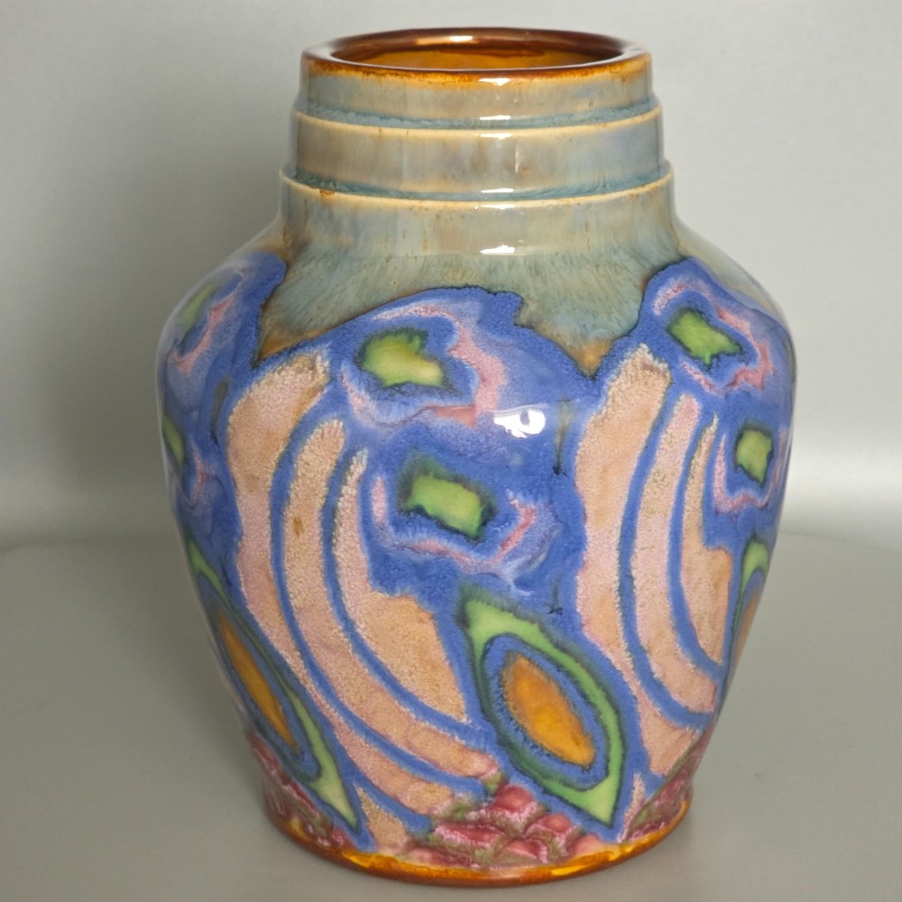 An Art Nouveau baluster-shaped stoneware vase with a stepped rim, featuring vibrant blue, pink, green, and ochre glazes forming abstract floral motifs.