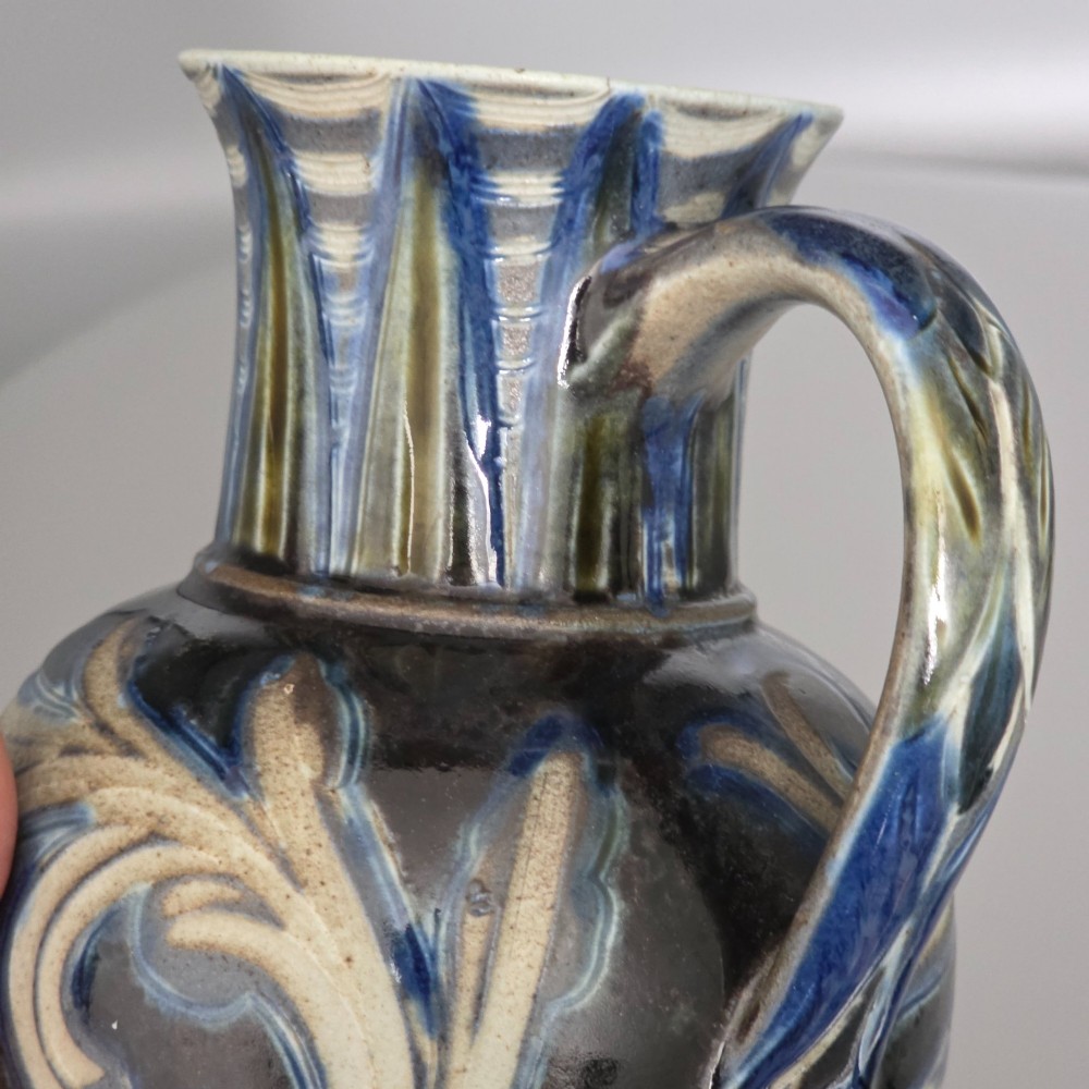 A Victorian salt-glazed stoneware jug decorated with incised blue and cream foliage patterns, a ribbed neck, and a loop handle against a dark brown ground. View III