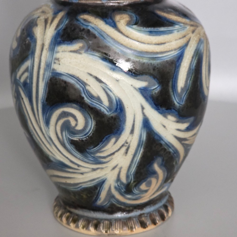 A Victorian salt-glazed stoneware jug decorated with incised blue and cream foliage patterns, a ribbed neck, and a loop handle against a dark brown ground. View IV