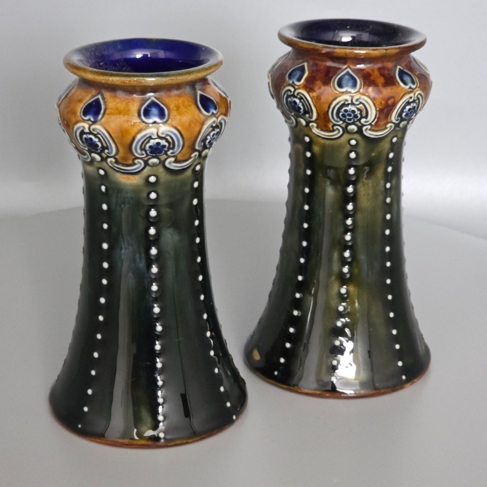 A pair of 1920s Royal Doulton Art Nouveau stoneware vases featuring flared bases, mottled dark green and brown glazes, and beaded shoulder decorations with blue accents.