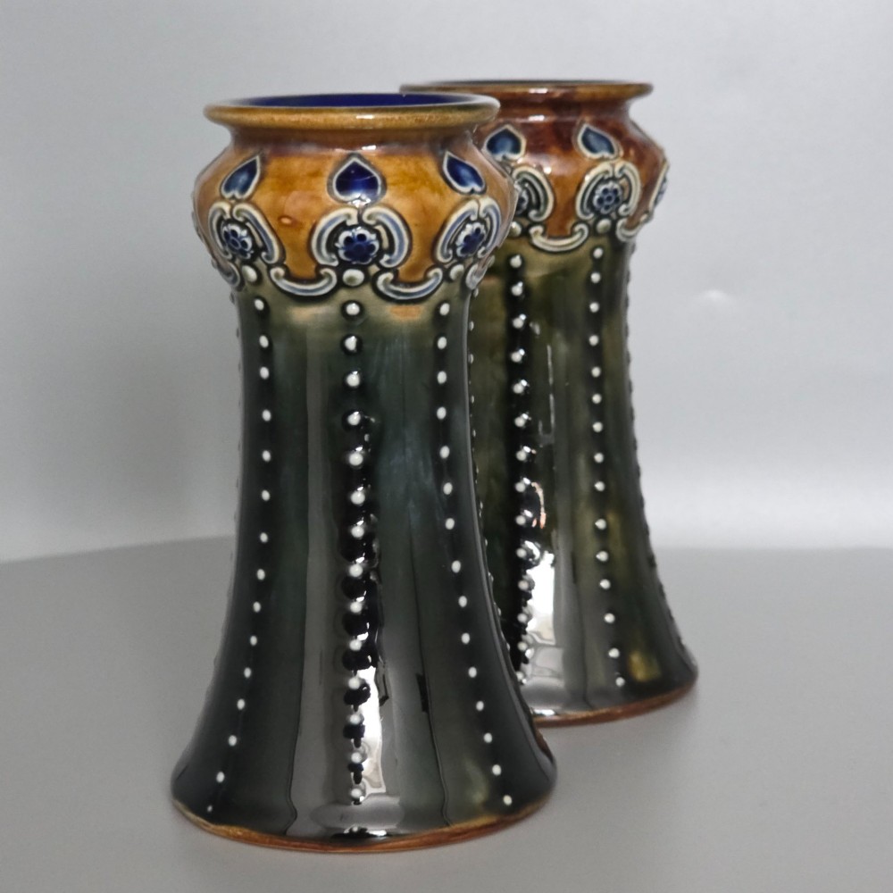 A pair of 1920s Royal Doulton Art Nouveau stoneware vases featuring flared bases, mottled dark green and brown glazes, and beaded shoulder decorations with blue accents. View V