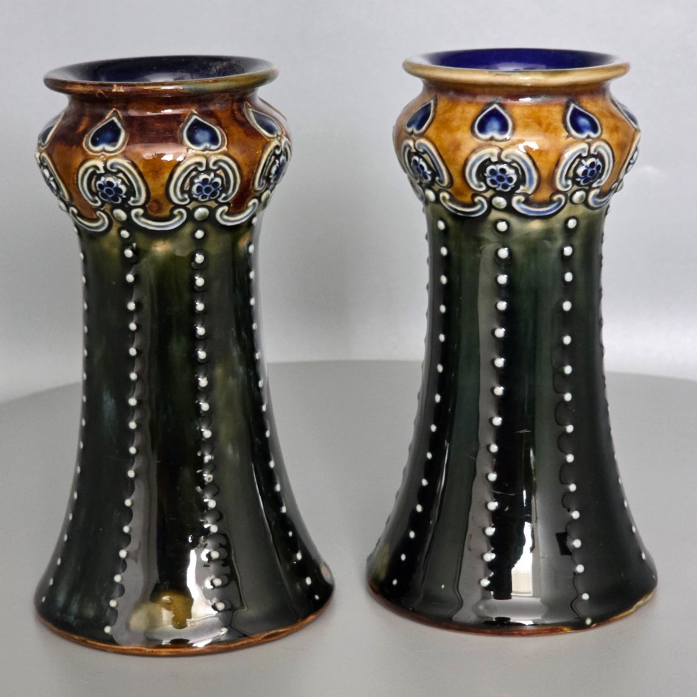 A pair of 1920s Royal Doulton Art Nouveau stoneware vases featuring flared bases, mottled dark green and brown glazes, and beaded shoulder decorations with blue accents. View VI