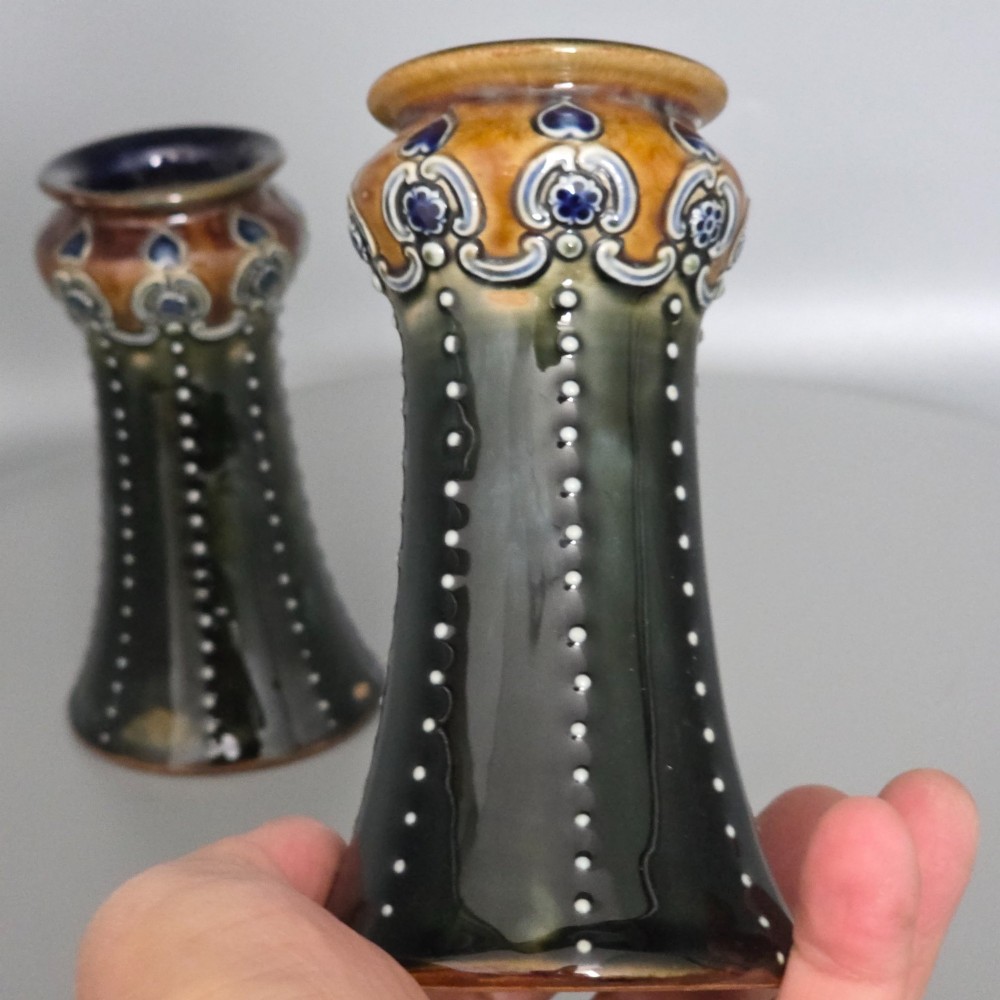 A pair of 1920s Royal Doulton Art Nouveau stoneware vases featuring flared bases, mottled dark green and brown glazes, and beaded shoulder decorations with blue accents. View VII