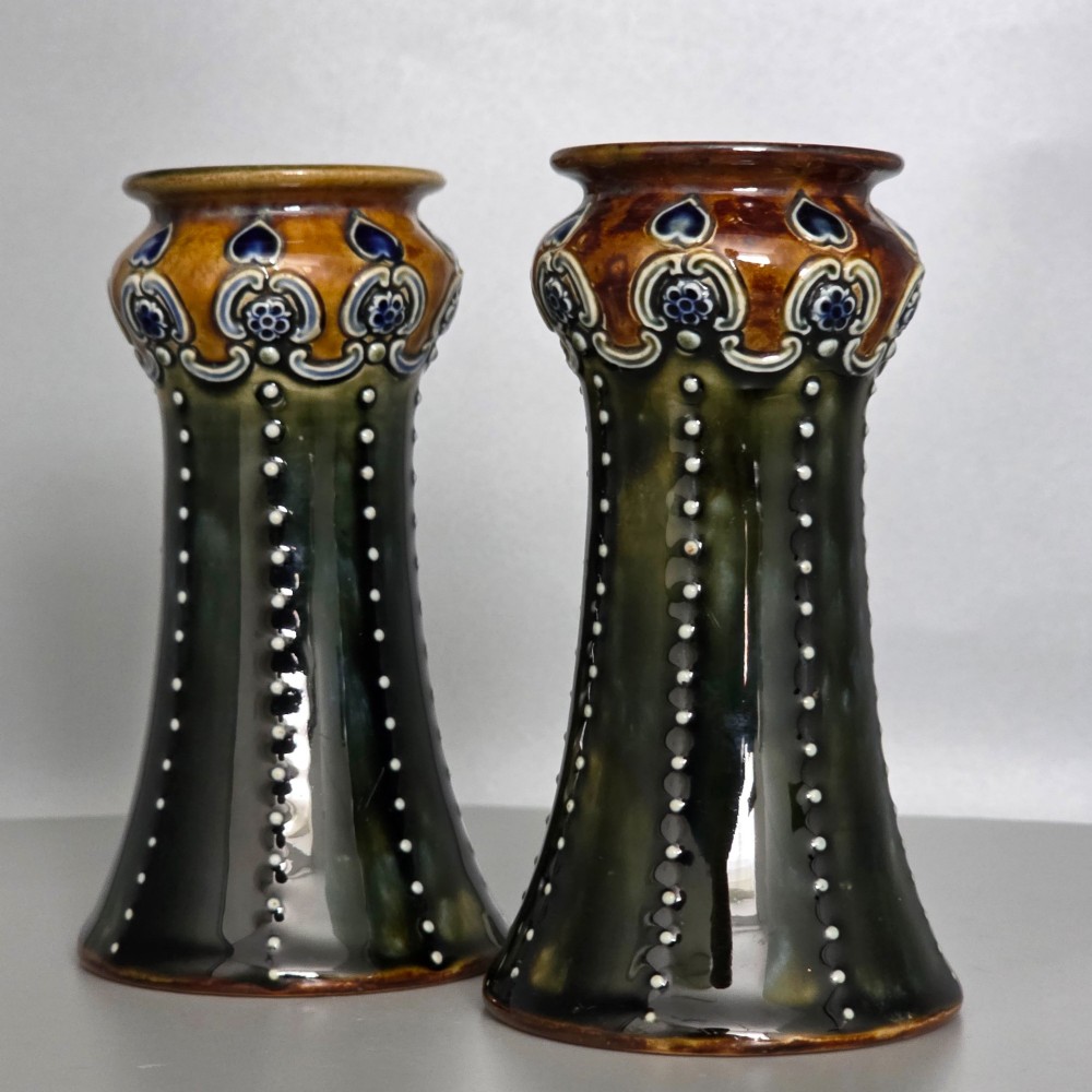 A pair of 1920s Royal Doulton Art Nouveau stoneware vases featuring flared bases, mottled dark green and brown glazes, and beaded shoulder decorations with blue accents. View XI