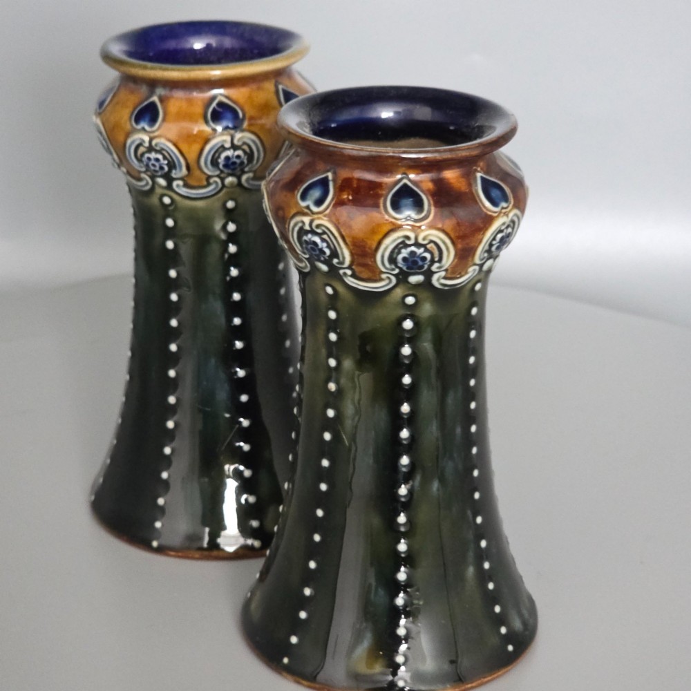 A pair of 1920s Royal Doulton Art Nouveau stoneware vases featuring flared bases, mottled dark green and brown glazes, and beaded shoulder decorations with blue accents. View XII