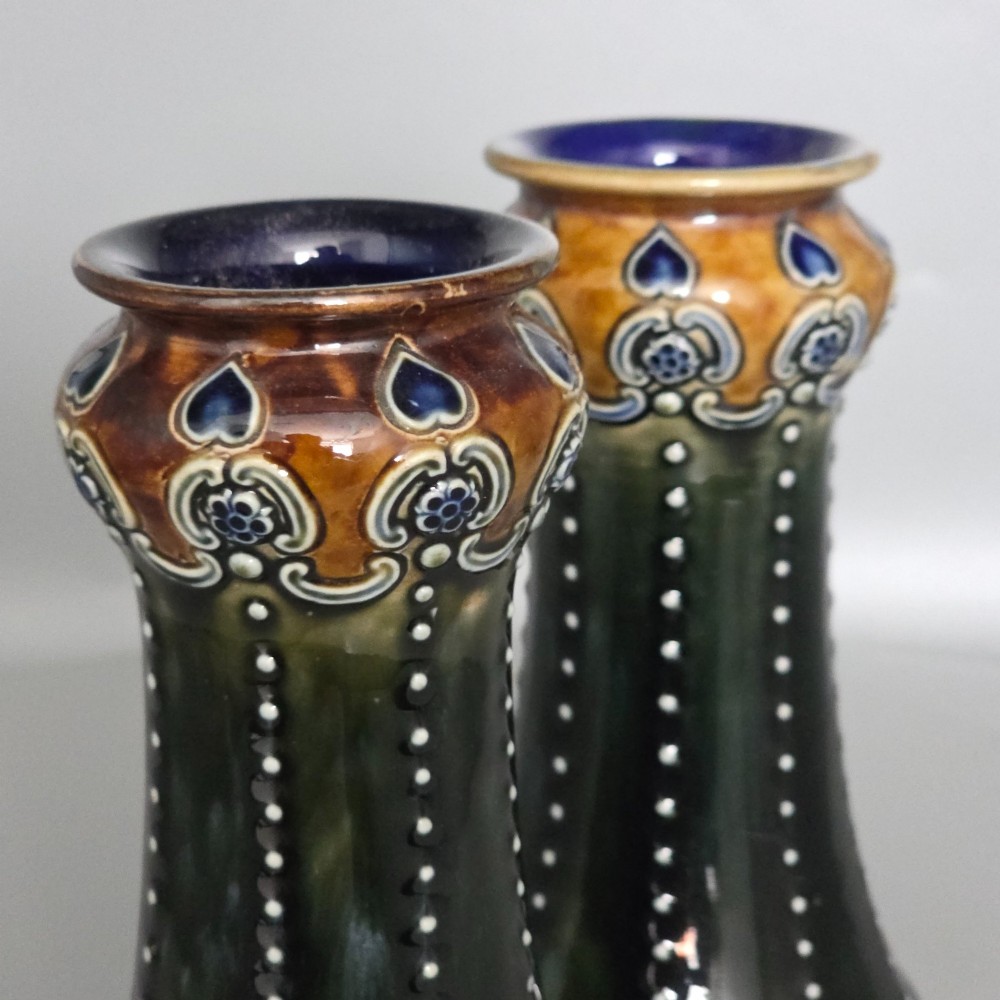 A pair of 1920s Royal Doulton Art Nouveau stoneware vases featuring flared bases, mottled dark green and brown glazes, and beaded shoulder decorations with blue accents. View XIV