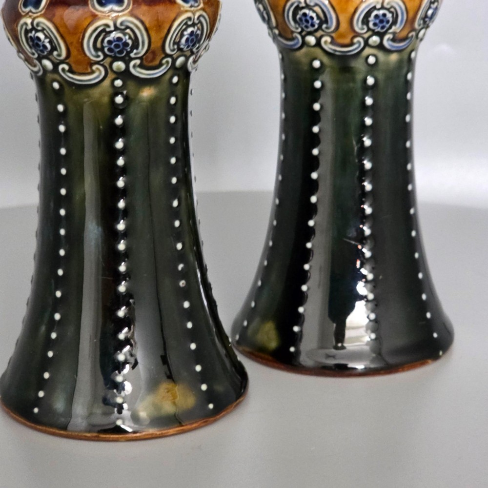 A pair of 1920s Royal Doulton Art Nouveau stoneware vases featuring flared bases, mottled dark green and brown glazes, and beaded shoulder decorations with blue accents. View XV