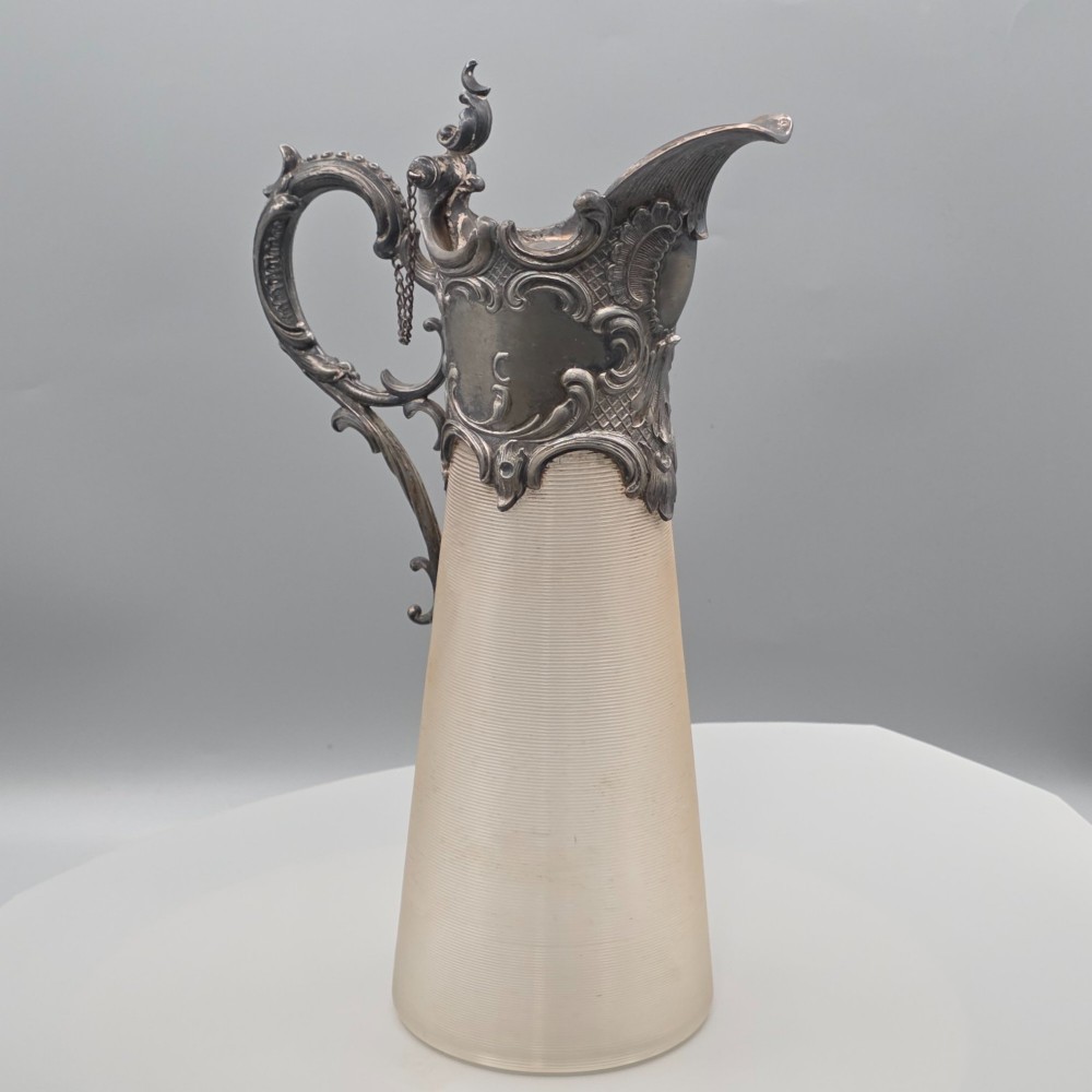 An antique French Rococo style silver-plated claret jug featuring a tapered ribbed clear glass body and an ornate scrolling silver spout and handle. View V