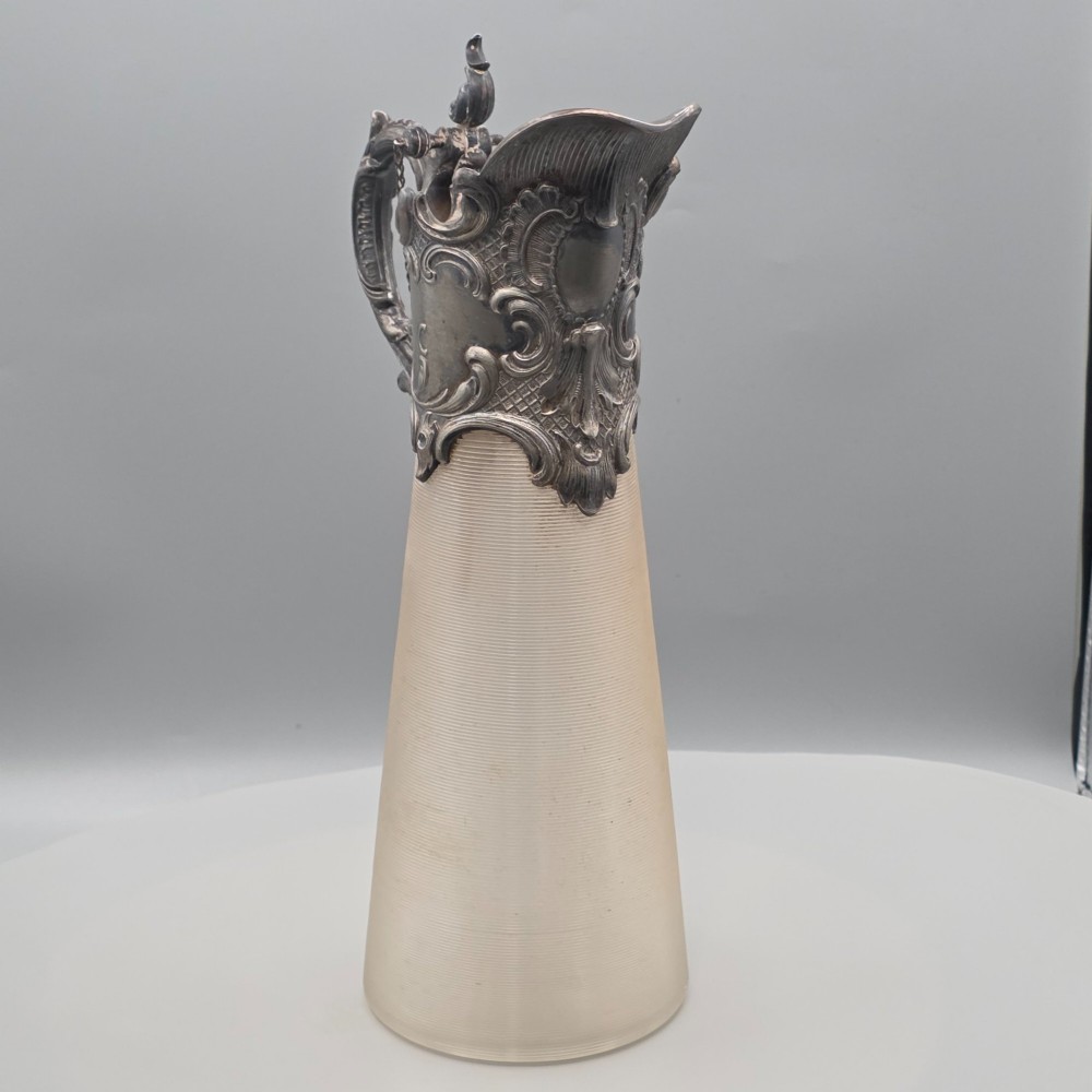 An antique French Rococo style silver-plated claret jug featuring a tapered ribbed clear glass body and an ornate scrolling silver spout and handle. View VI