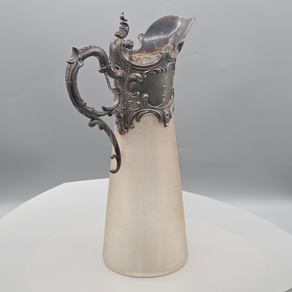 An antique French Rococo style silver-plated claret jug featuring a tapered ribbed clear glass body and an ornate scrolling silver spout and handle. View VII