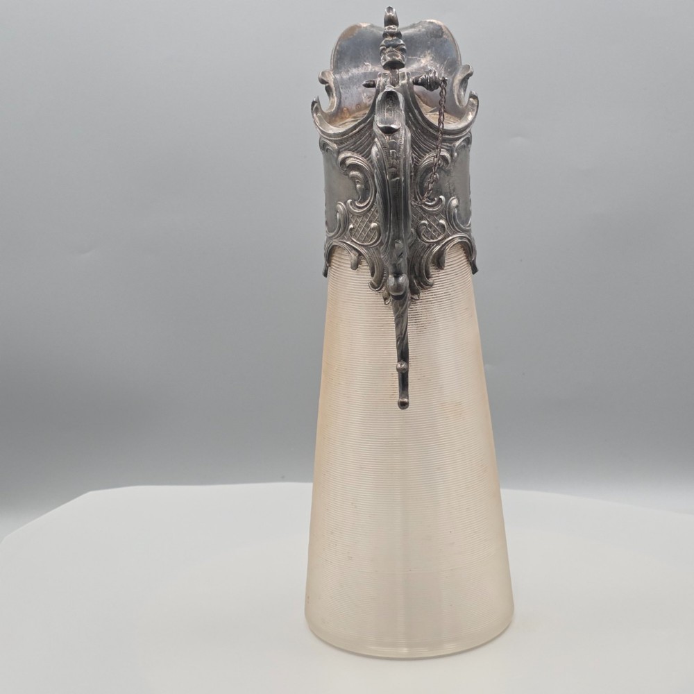 An antique French Rococo style silver-plated claret jug featuring a tapered ribbed clear glass body and an ornate scrolling silver spout and handle. View VIII